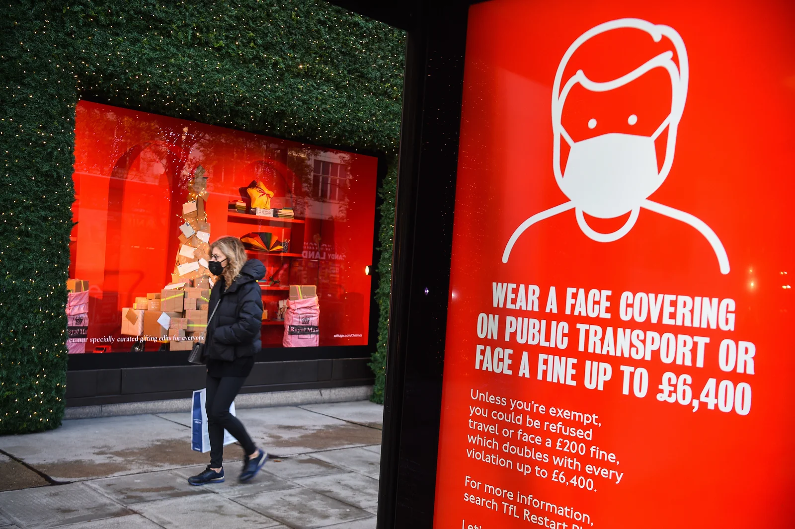A woman wearing a face mask passing a screen advising the wearing of face masks on Oxford Street | PA